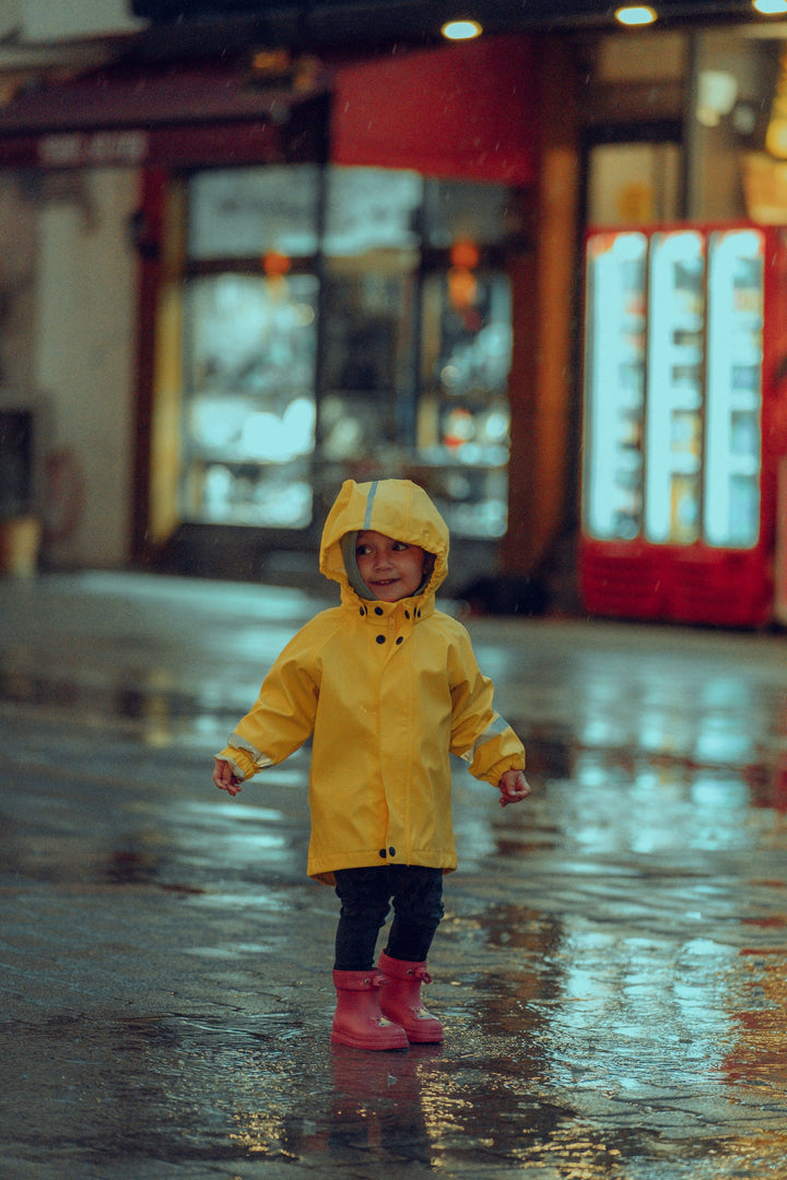 Child in a yellow hooded rain poncho on a rainy street